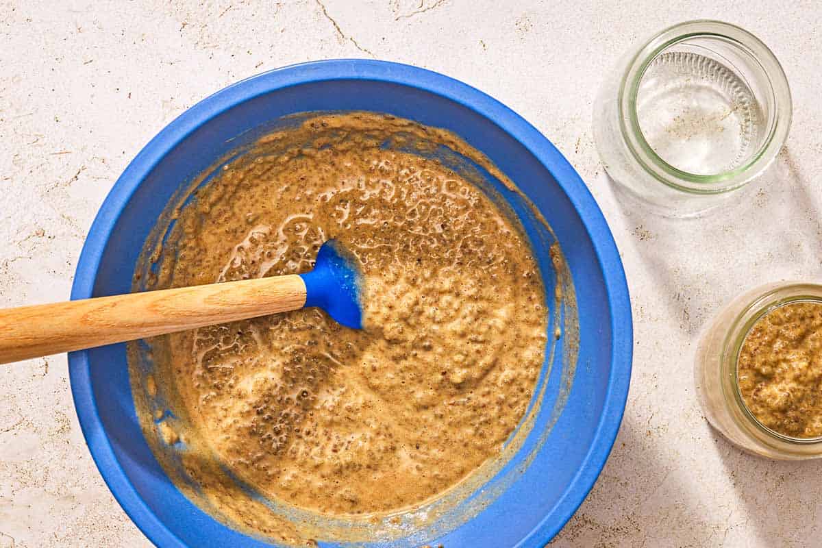 The chia seed pudding in a mixing bowl with a spatula. Next to this is one empty jar, and one jar filled with the pudding.