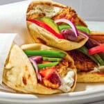 Three chicken gyros on a plate, each one wrapped in parchment paper.