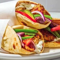 Three chicken gyros on a plate, each one wrapped in parchment paper.