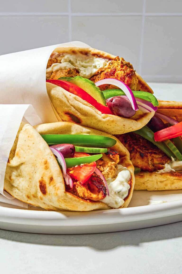 Three chicken gyros on a plate, each one wrapped in parchment paper.
