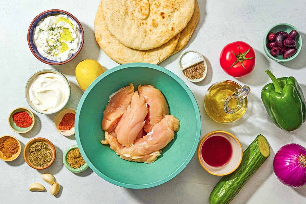 Ingredients for the chicken gyro recipe including chicken tenders, greek yogurt, lemon, olive oil, red wine vinegar, garlic, oregano, sweet paprika, cumin, coriander, cayenne pepper, salt, black pepper, pita bread, tzatziki sauce, tomato, cucumber, red onion and kalamata olives.