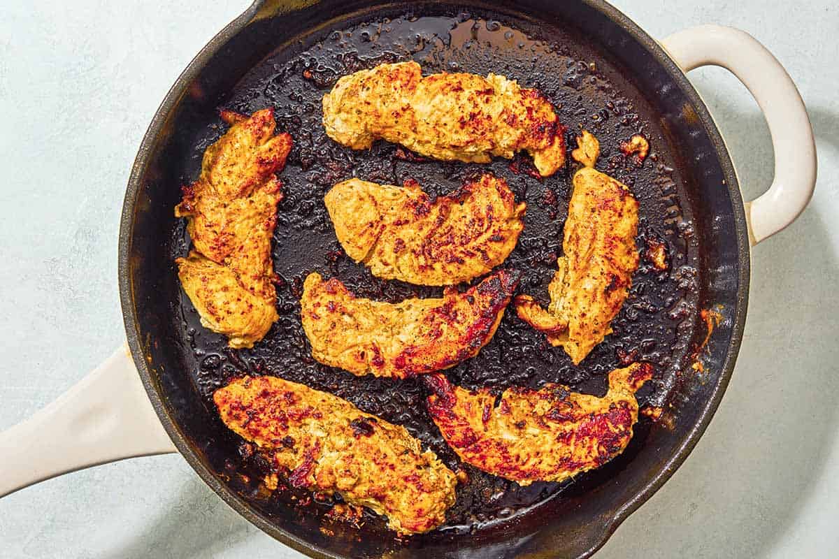 The chicken tenders for the chicken gyro recipe being cooked in a skillet.
