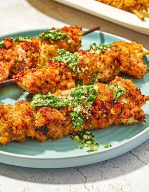 Three chicken spiedini skewers topped with the garlic parmesan herb sauce on a plate.