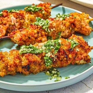 Three chicken spiedini skewers topped with the garlic parmesan herb sauce on a plate.
