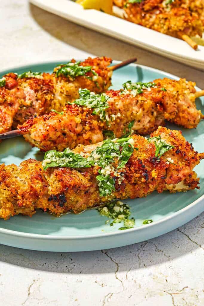 Three chicken spiedini skewers topped with the garlic parmesan herb sauce on a plate.
