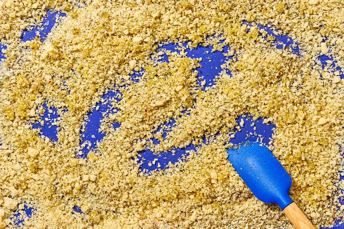 Breadcrumbs spread evenly on a sheet pan with a spatula.
