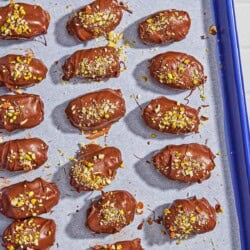 Several chocolate covered dates spread evenly on a parchment lined sheet pan.