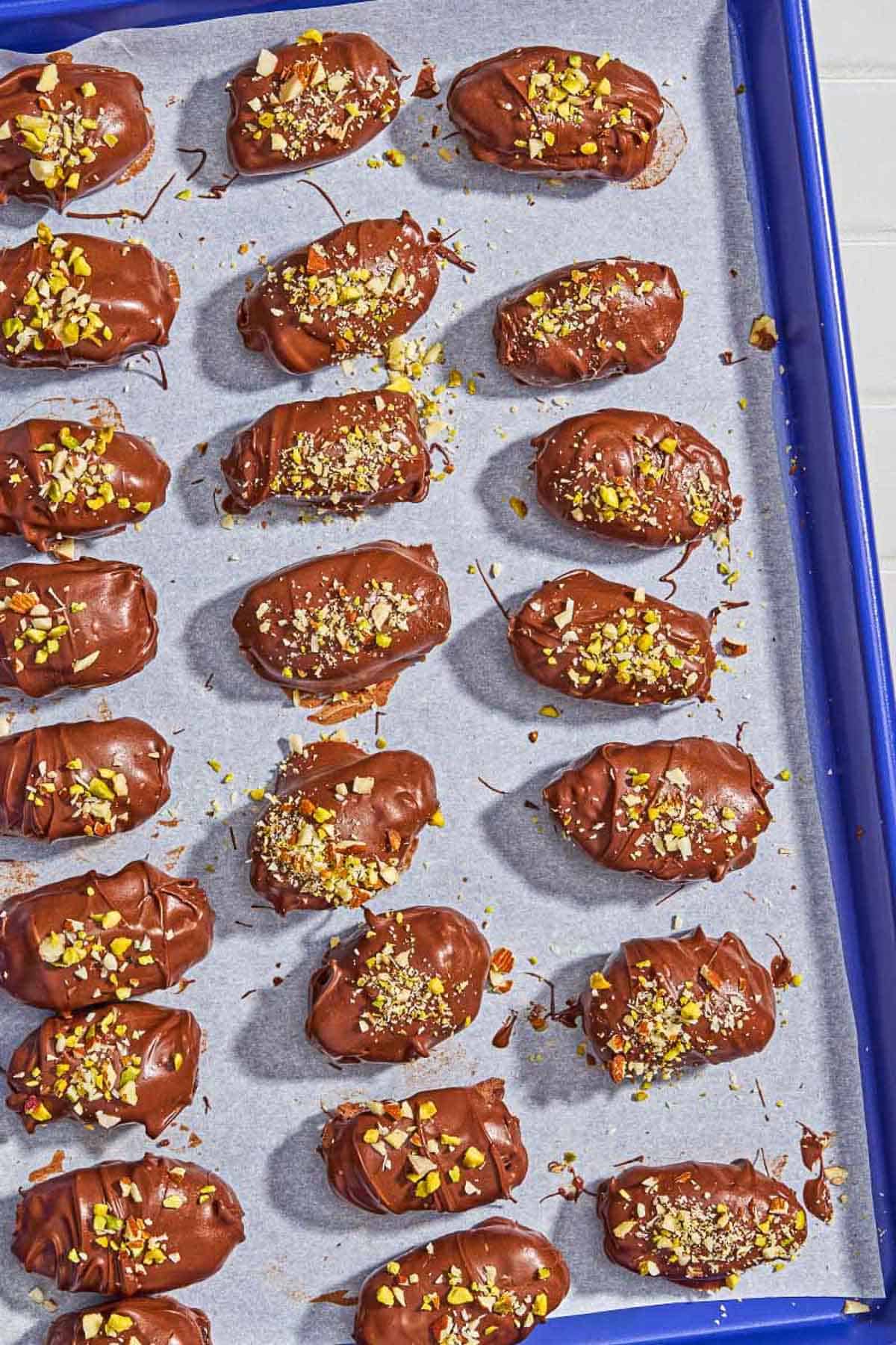 Several chocolate covered dates spread evenly on a parchment lined sheet pan.