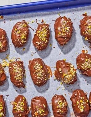 Several chocolate covered dates spread evenly on a parchment line sheet pan.