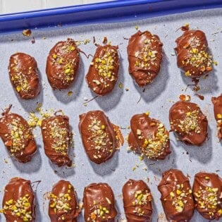 Several chocolate covered dates spread evenly on a parchment line sheet pan.