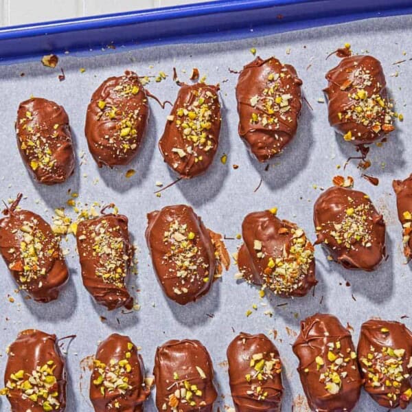 Several chocolate covered dates spread evenly on a parchment line sheet pan.