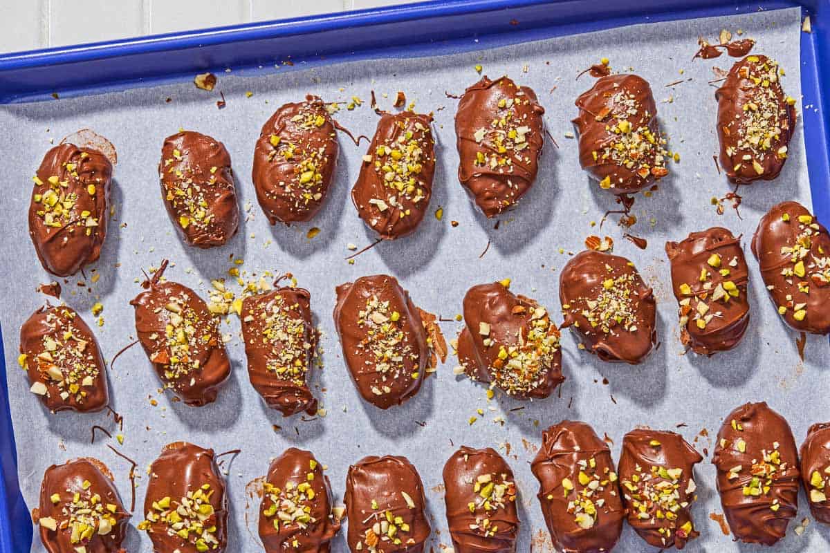 Several chocolate covered dates spread evenly on a parchment line sheet pan.