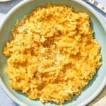 Risotto in a bowl next to a fork, a cloth napkin and a small bowl of Parmigiano-Reggiano cheese.