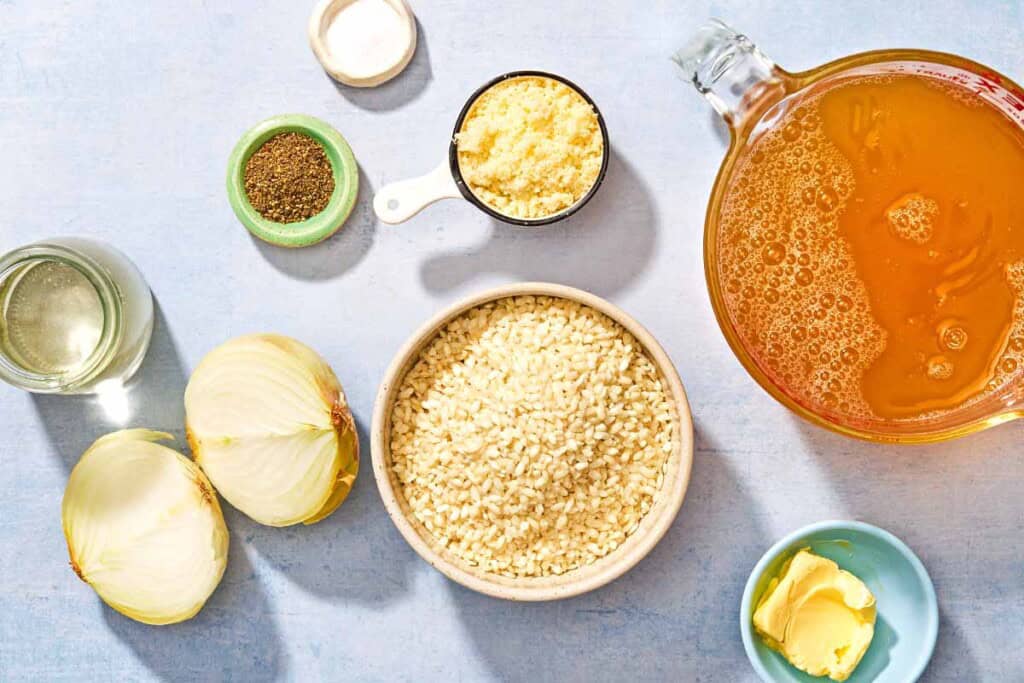 Ingredients for risotto including arborio rice, chicken stock, butter, onion. salt, white wine, grated Parmigiano-Reggiano cheese, and black pepper.