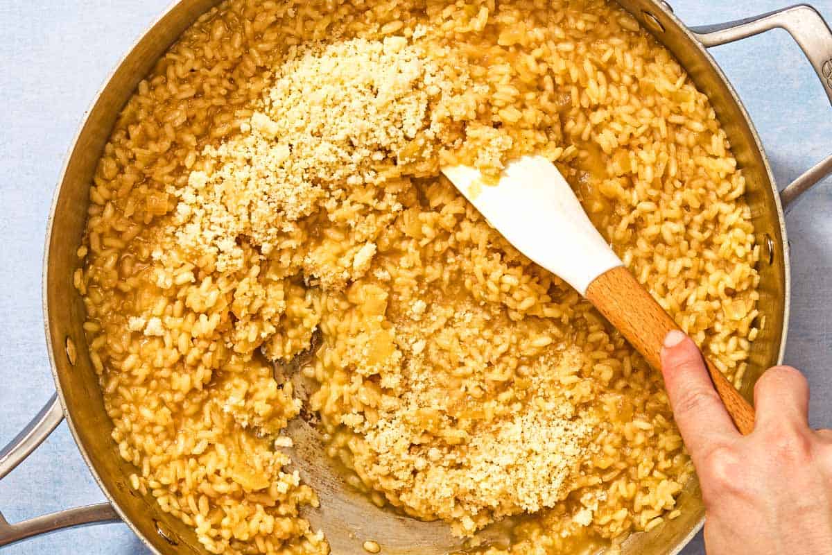 Grated Parmigiano-Reggiano cheese being stirred into the risotto in the deep skillet as a finishing touch.