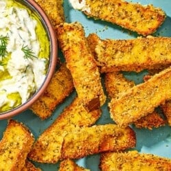Eggplant fries on a platter with a small bowl of tzatziki sauce.