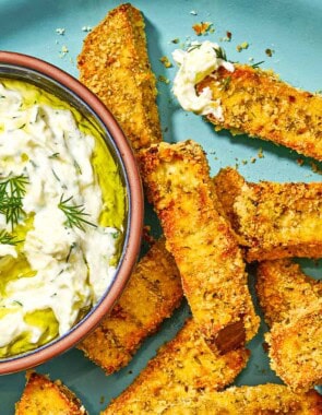 Eggplant fries on a platter with a small bowl of tzatziki sauce.