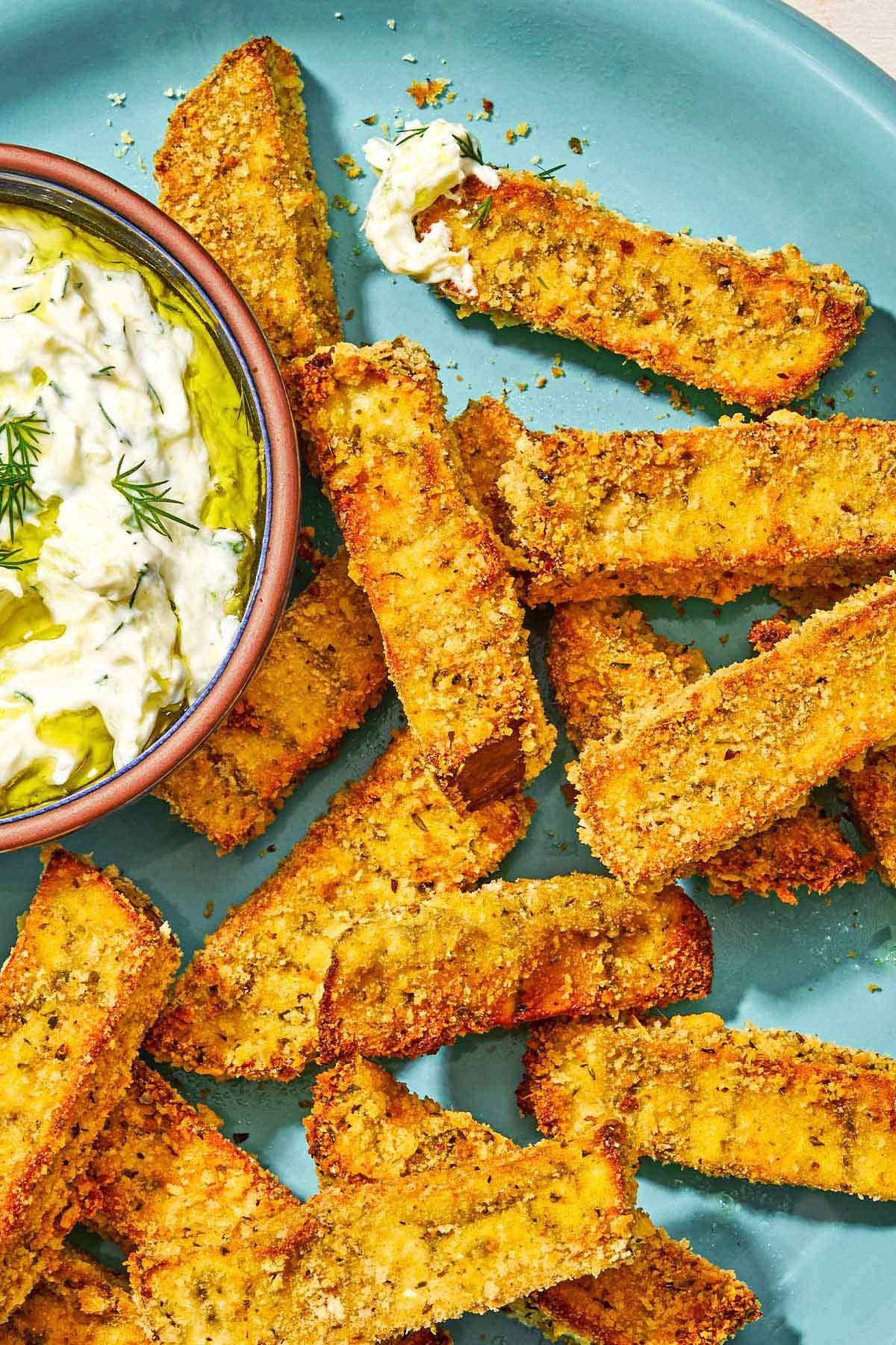 Eggplant fries on a platter with a small bowl of tzatziki sauce.