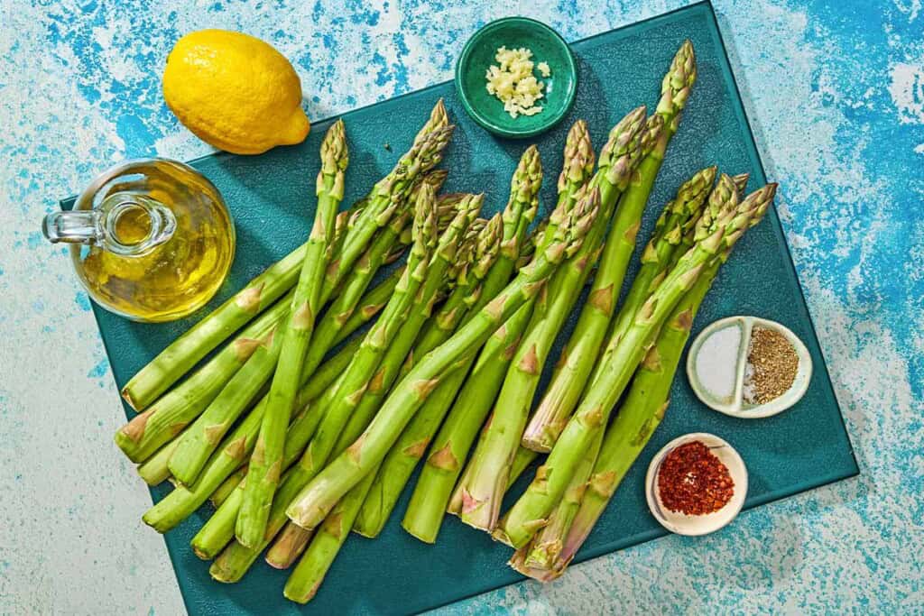 Ingredients for grilled asparagus including asparagus, olive oil, garlic, lemon, salt, black pepper, and aleppo pepper.