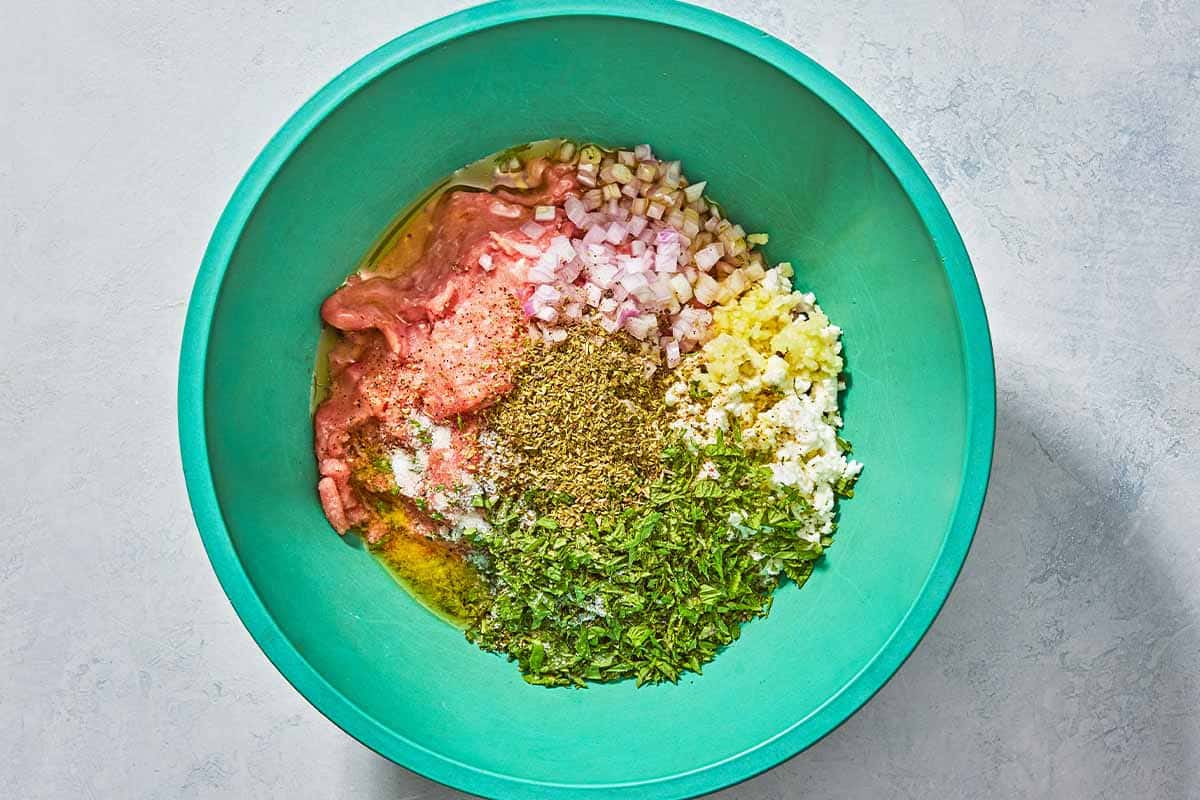 The ground turkey, chopped shallot mint and garlic, crumbled feta , oregano, black pepper and salt in a bowl, just before being mixed together.
