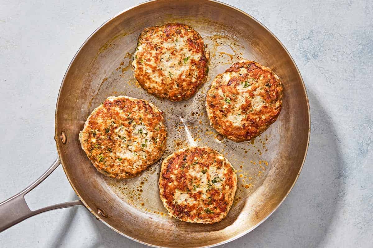 4 turkey burger patties cooking in a skillet.