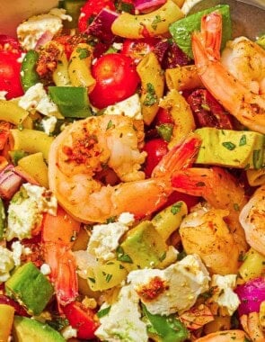 A bowl of shrimp pasta salad with a serving spoon next to a cloth napkin and a plate.