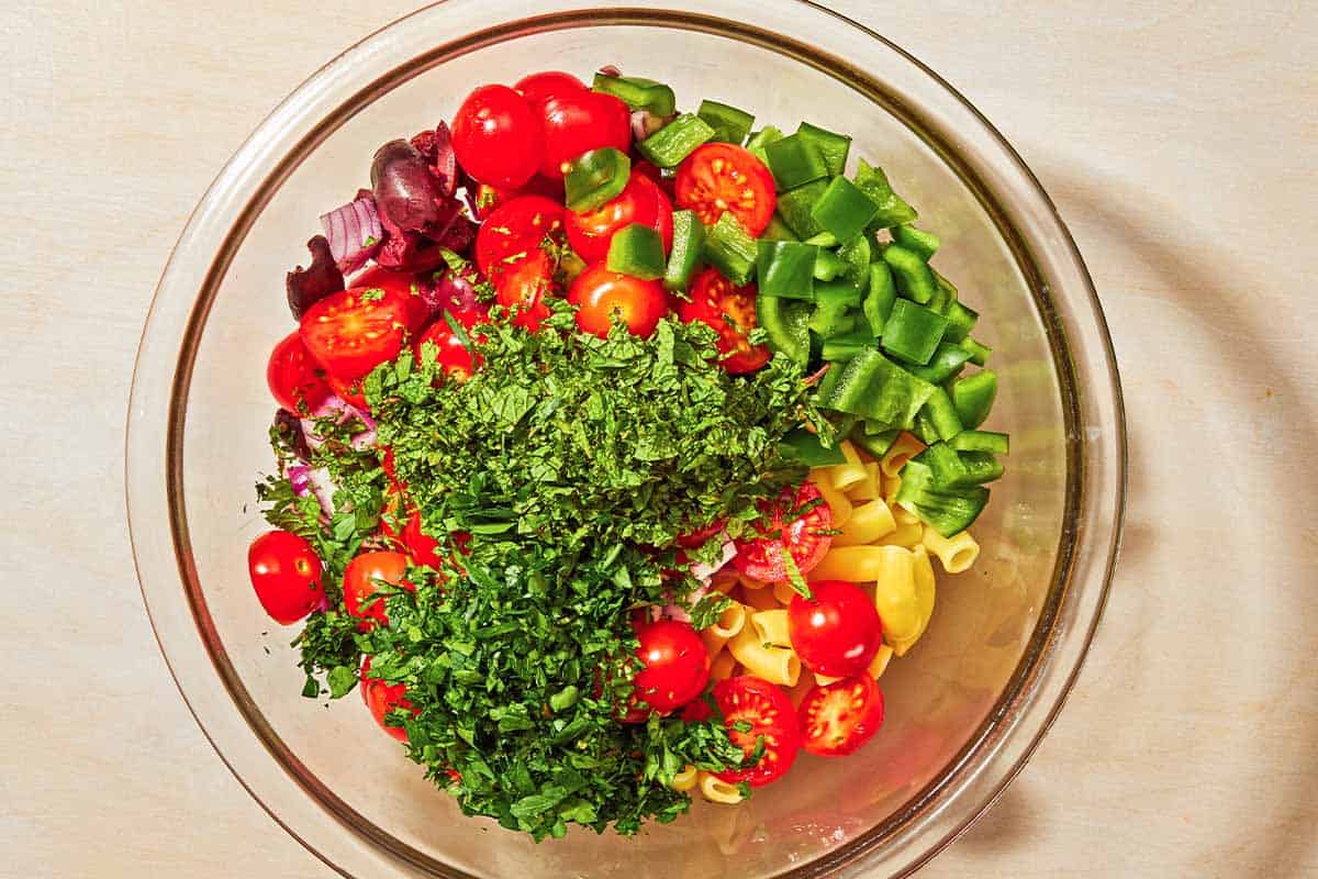 The pasta, vegetables and herbs for the pasta salad in a bowl just before being mixed together.