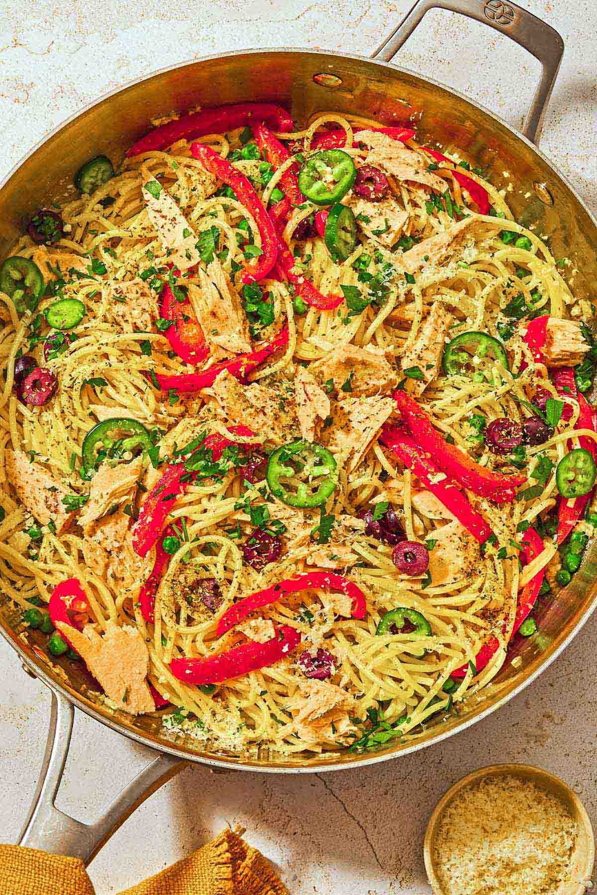 Tuna pasta in a deep skillet next to a small bowl of grated Parmesan cheese.