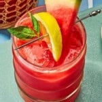 A glass of watermelon lemonade garnished with basil and slices of watermelon and lemon.