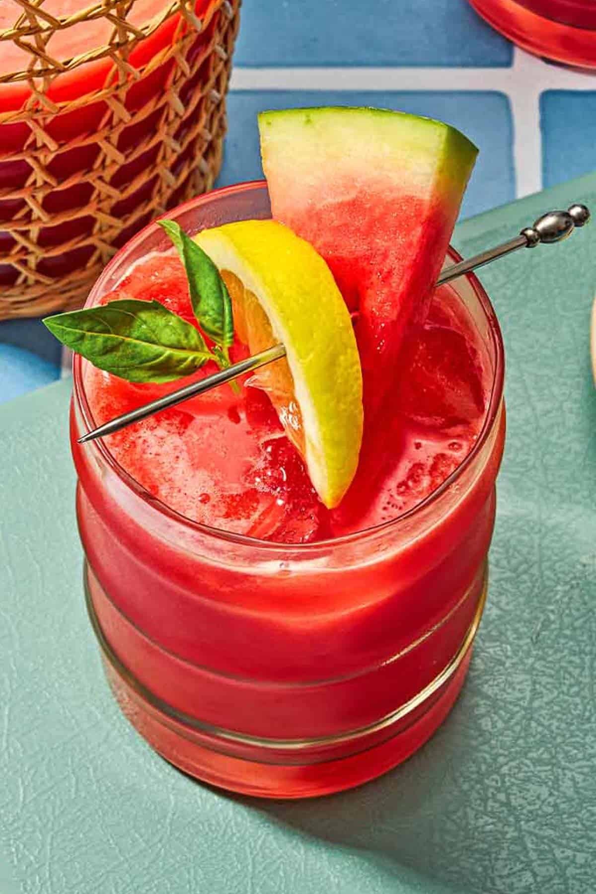 A glass of watermelon lemonade garnished with basil and slices of watermelon and lemon.