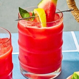 A glass of watermelon lemonade garnished with basil and slices of watermelon and lemon.