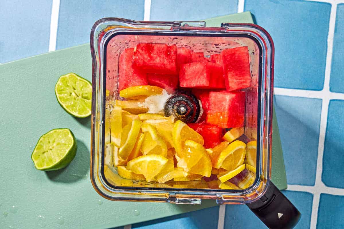 The ingredients for the watermelon lemonade in the pitcher of a blender just before being mixed together next to two juiced lime halves.