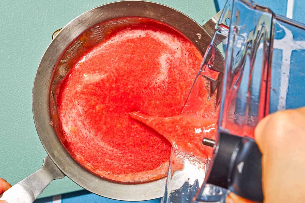The watermelon lemonade being poured into a fine mesh strainer over a pitcher.