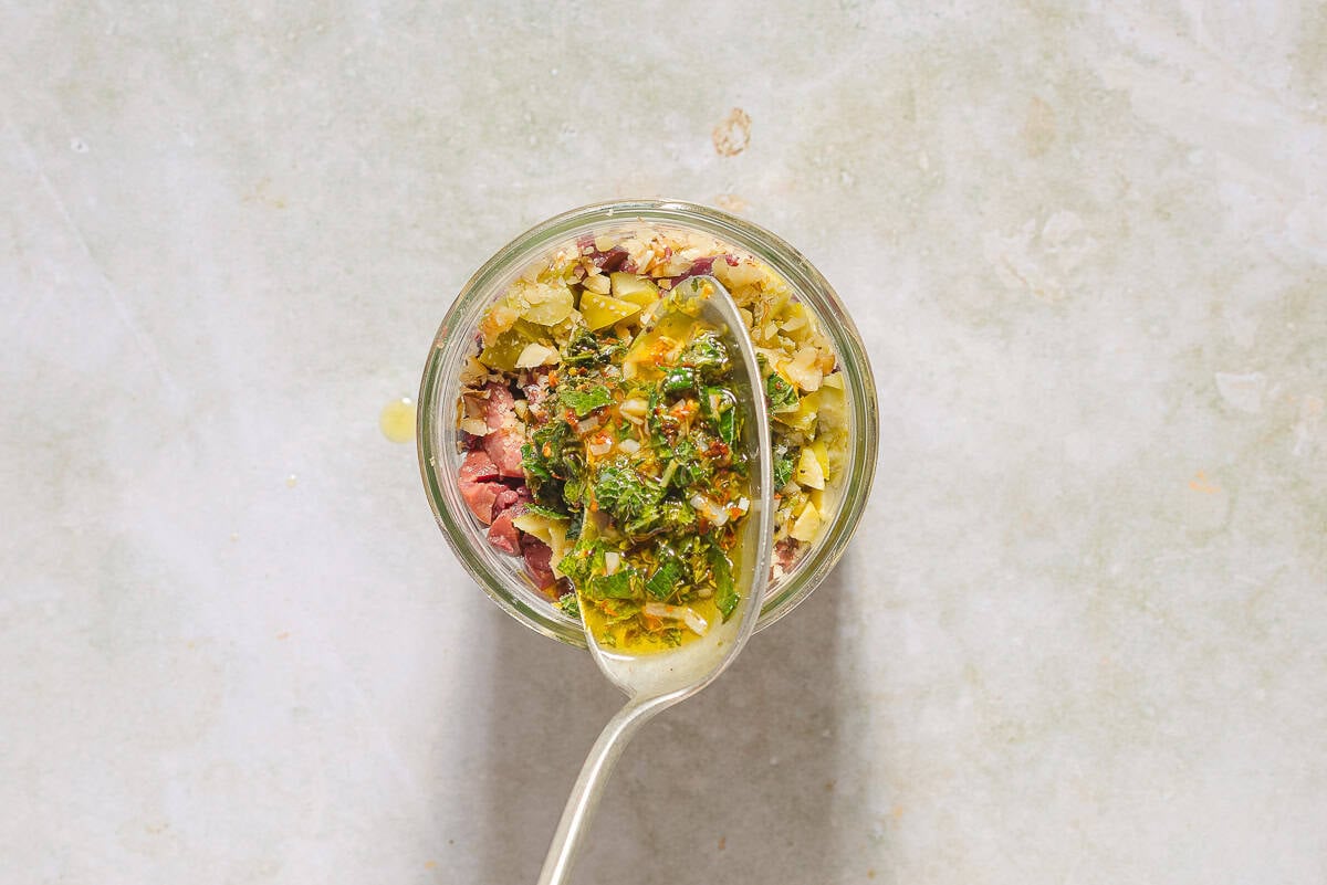 The warm marinade for the zeytoon parvardeh being stirred with the olives and walnuts in a wide mouthed mason jar.