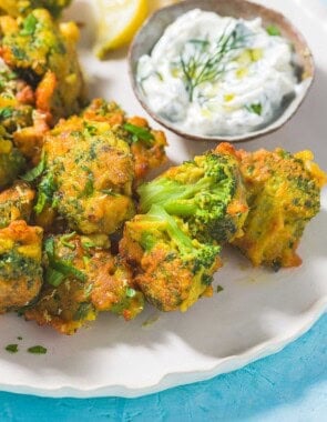 Broccoli Fritters on a plate with a small bowl of tzatziki sauce and lemon wedges.