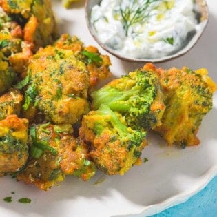 Broccoli Fritters on a plate with a small bowl of tzatziki sauce and lemon wedges.
