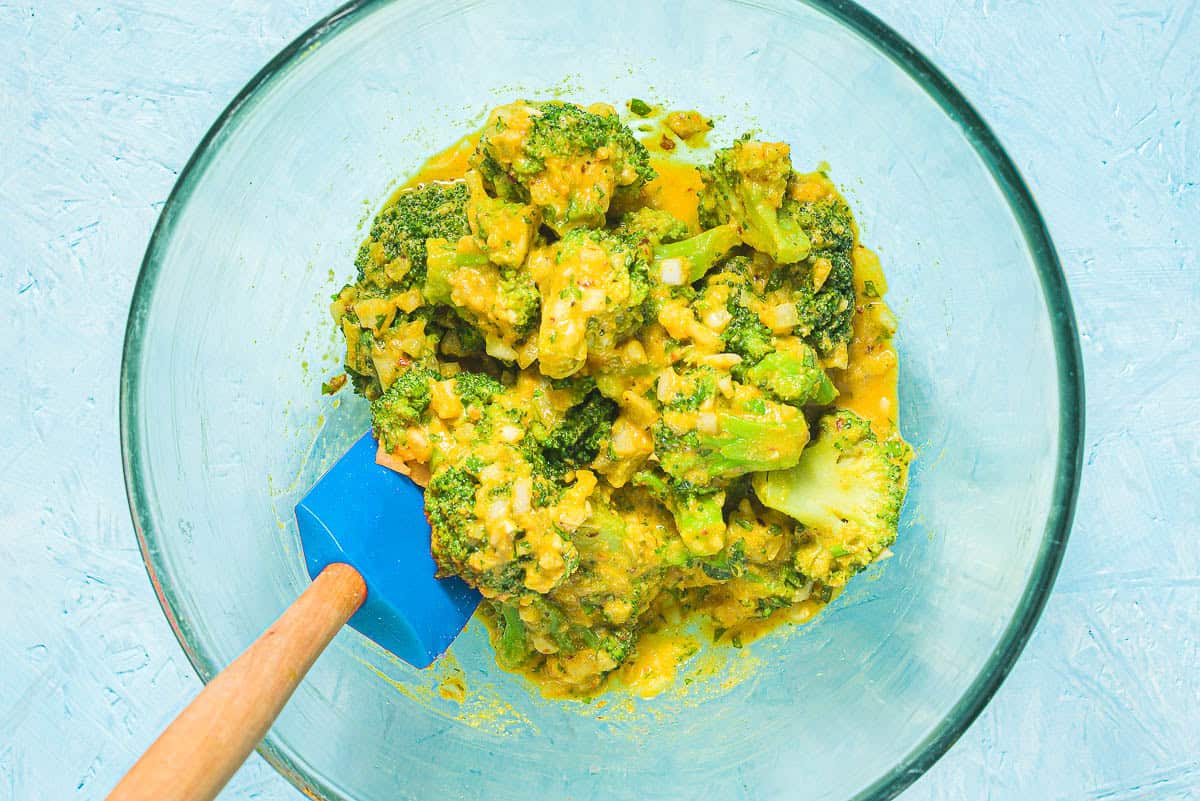 The ingredients for broccoli fritters being mixed together in a bowl with a spatula.
