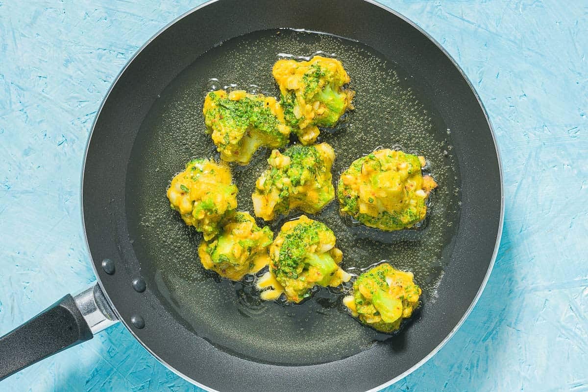 Broccoli fritters being sauteed in olive oil in a skillet.
