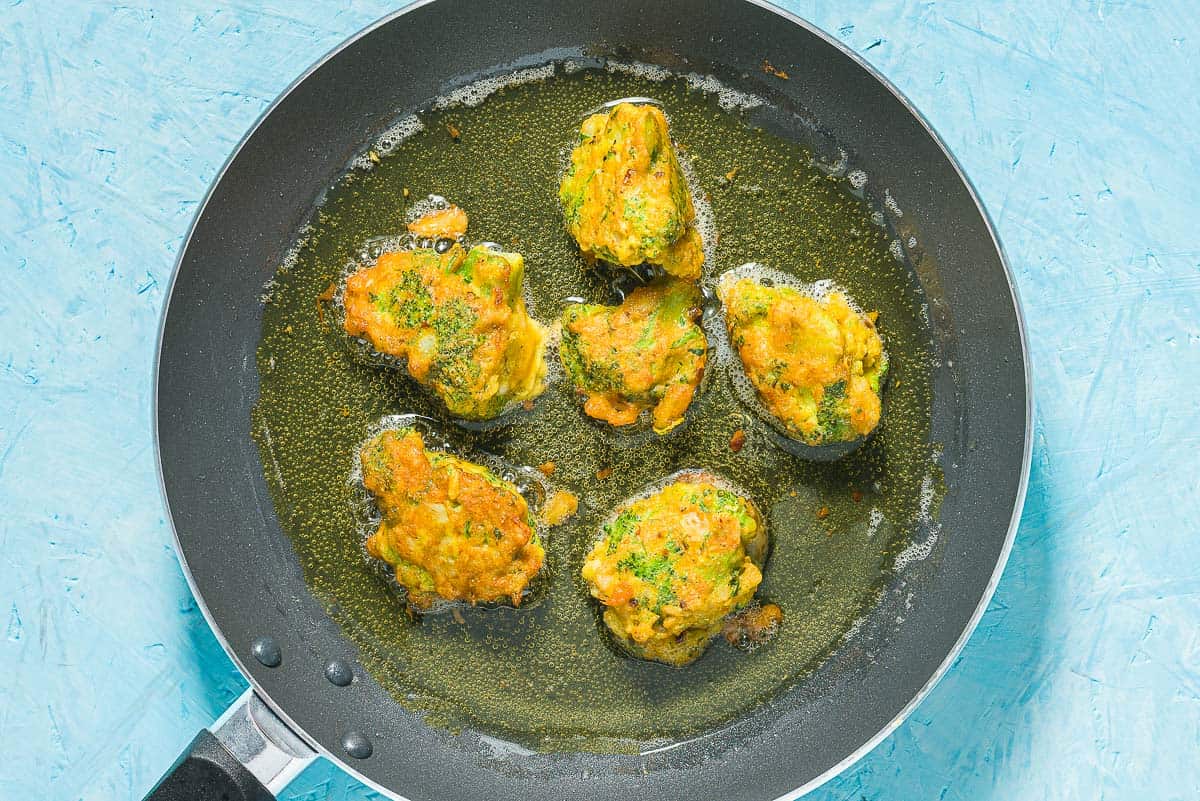 Broccoli fritters being sauteed in olive oil in a skillet.