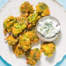 Broccoli Fritters on a plate with a small bowl of tzatziki sauce and lemon wedges.