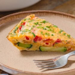 A slice of crustless zucchini quiche on a plate with a fork.