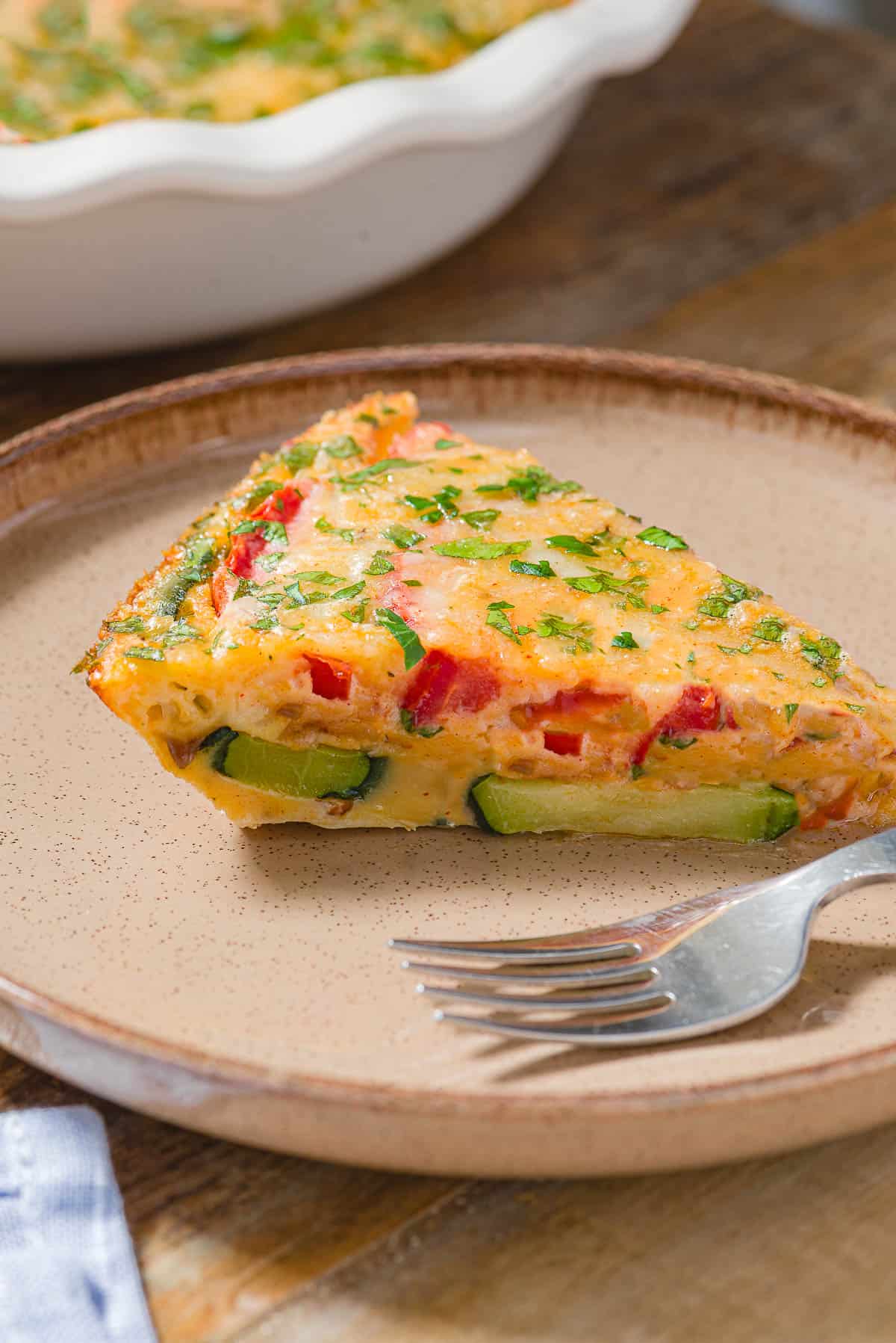 A slice of crustless zucchini quiche on a plate with a fork.