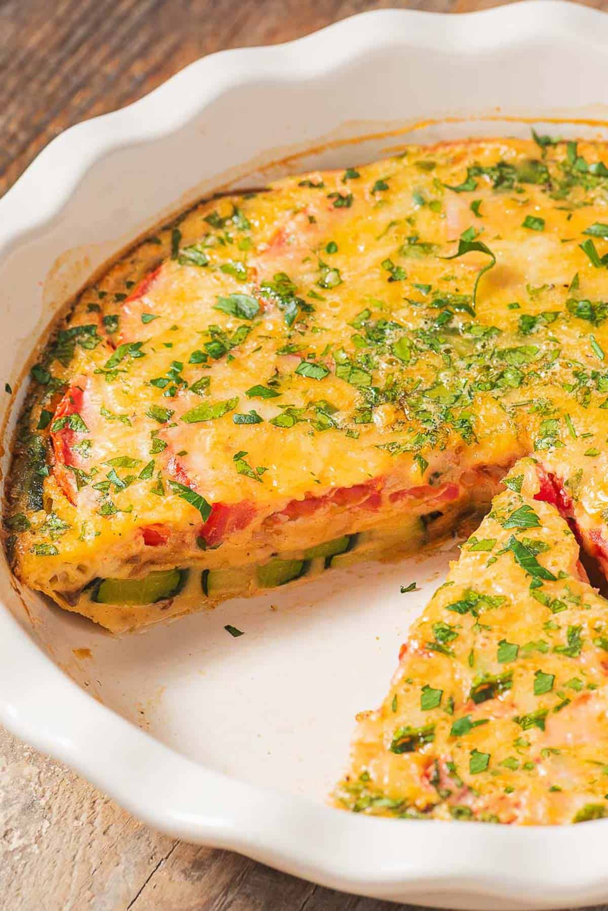 The crustless zucchini quiche in a baking dish with one slice removed.