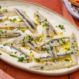 Boquerones on a platter next to a bowl of green olives.