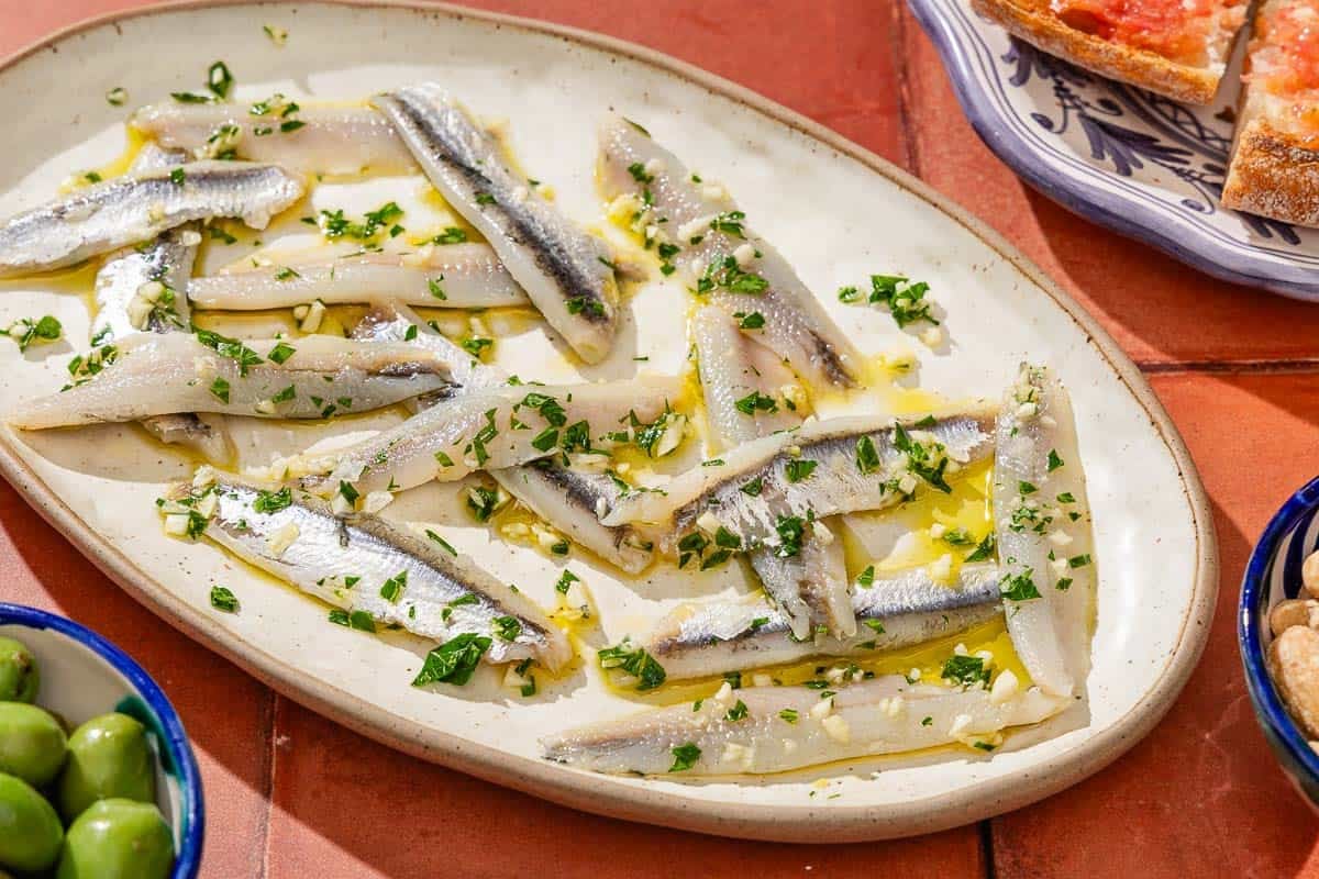 Boquerones on a platter next to a bowl of green olives.
