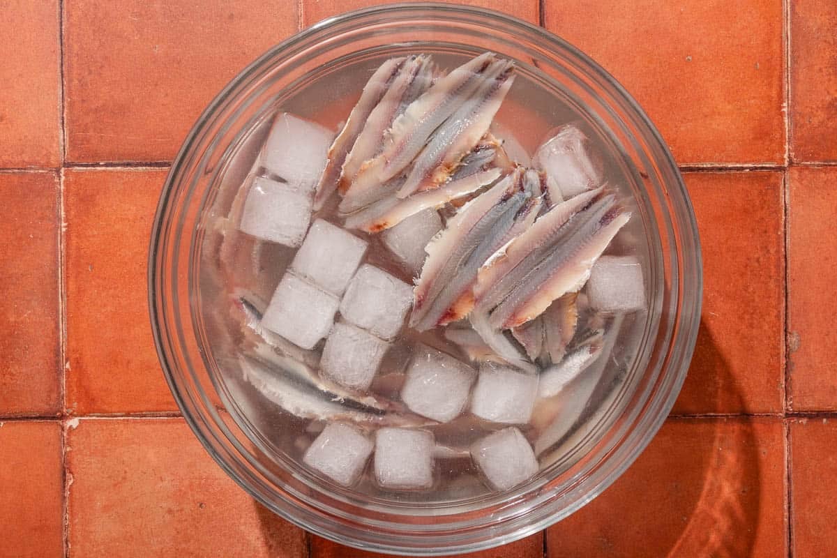 Anchovy fillets soaking in ice water in a bowl.