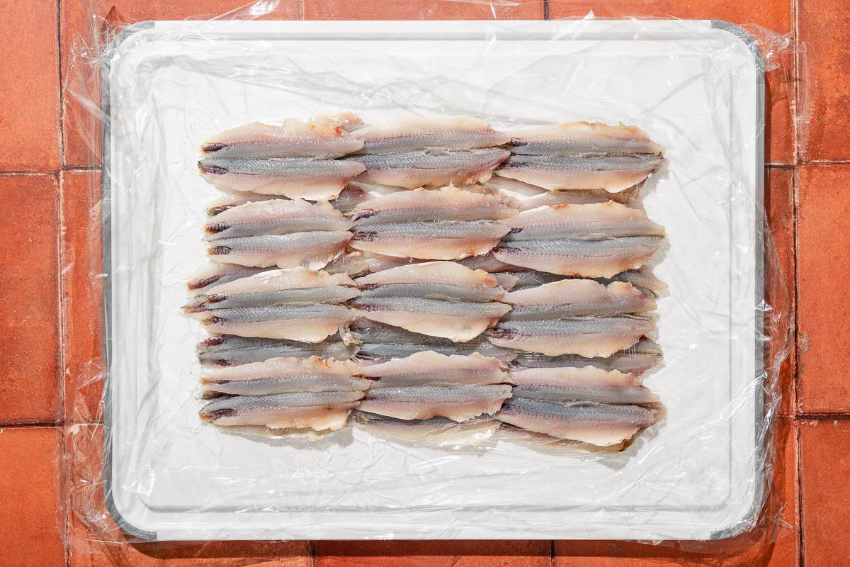 Cleaned anchovy fillets on a cutting board lined with plastic wrap.