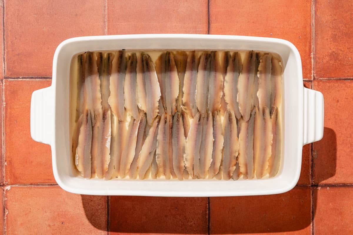 Anchovy fillets being pickled in a baking dish.