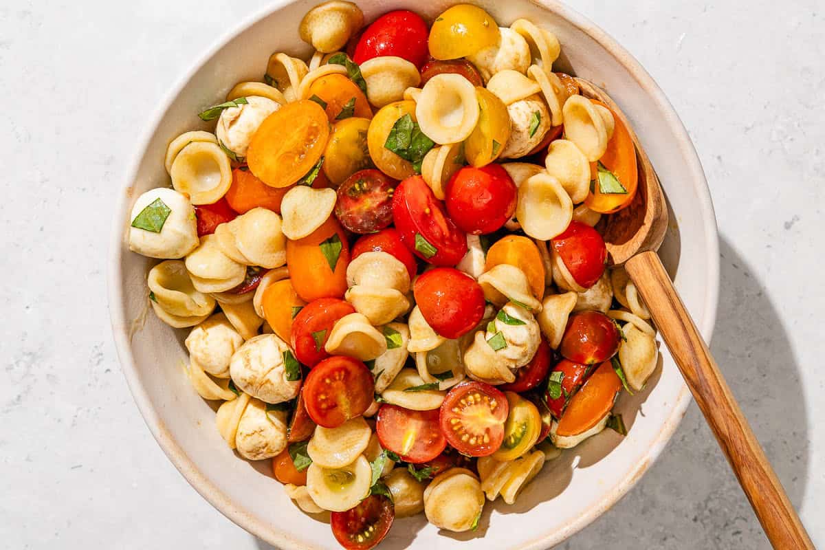 The caprese salad in a mixing bowl with a wooden spoon.