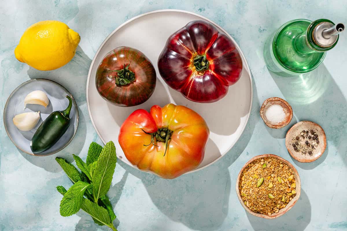 Ingredients for heirloom tomato salad including heirloom tomatoes, garlic, lemon, olive oil, salt, black pepper, a jalapeño pepper, dukkah, and mint.